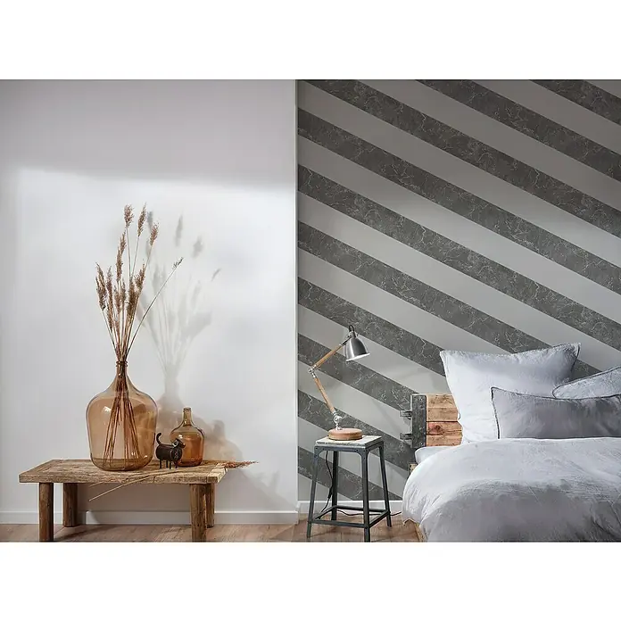 A.S. Création Michalsky 4 Vliestapete Marmor - Grau, Streifen, 10,05 x 0,53 m - Einrichtungsidee mit dekorativen Glasflaschen auf einem Holztisch und einem Bett mit grau gestreifter Wand im Hintergrund.