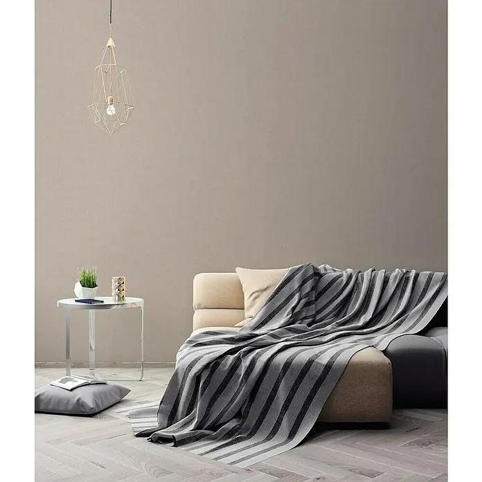 A.S. Création Titanium 3 Vliestapete - Cremiges Beige, Uni, 10,05 x 0,53 m - Ein stilvolles Wohnzimmer mit einer bequemen Couch, die mit einer gestreiften Tagesdecke bedeckt ist, und einer modernen Pendelleuchte.
