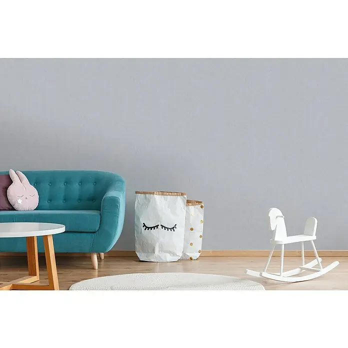 A.S. Création Titanium 3 Vliestapete - Wohnliches Grau, Uni, 10,05 x 0,53 m - Helle, freundliche Kinderzimmer-Szene mit türkisfarbenem Sofa, weißem Tisch, Spielzeug und dekorativen Aufbewahrungstaschen.