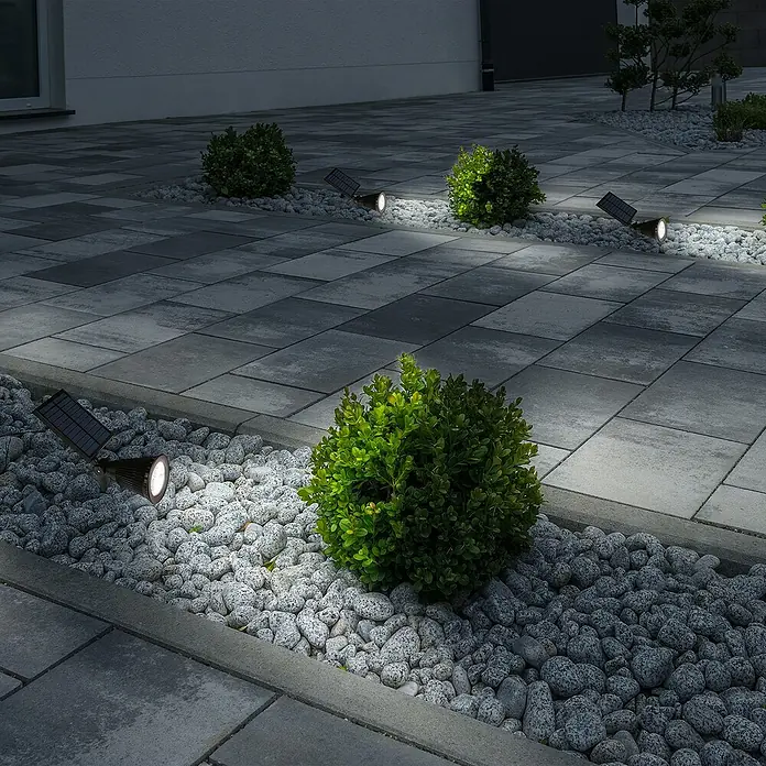 Arte confort Foco solar Corvus - 2 W, L x An x Al: 27 x 9,5 x 32 cm, Negro - Vista del jardín con focos solares que iluminan arbustos y un camino pavimentado.