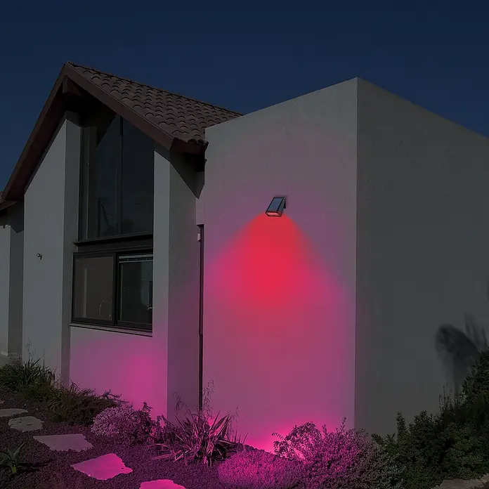 Arte confort Aplique solar para exterior Perseo - 2 W, L x An x Al: 11,7 x 8 x 16,9 cm, Negro, IP65, 200 lm - Una pared de la casa está iluminada por una luz solar roja, creando un ambiente atmosférico.