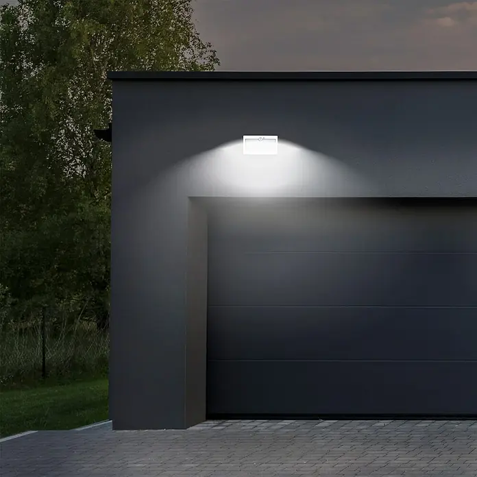 Arte confort Aplique solar para exterior Osiris - L x An x Al: 11,5 x 22 x 6 cm, Blanco, IP54, 900 lm - Luz exterior brillante fijada a un garaje gris. Emite una luz fuerte, iluminando el área inferior para mayor seguridad.