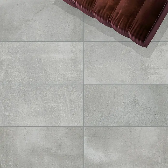 Feinsteinzeugfliese Manhattan Smoke - 30 x 60 cm, Grau, Matt - Graue Bodenfliesen in einem klaren, modernen Design, teilweise von einem braunen Möbelstück bedeckt, schaffen eine stilvolle Atmosphäre.