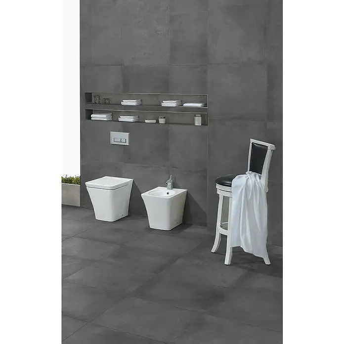Feinsteinzeugfliese Manhattan Dark - 60 x 60 cm, Anthrazit, Matt - Stilvolles Badezimmer mit moderner Toilette und Bidet in Weiß, ergänzt durch ein elegantes Regal und einen dekorativen Stuhl.