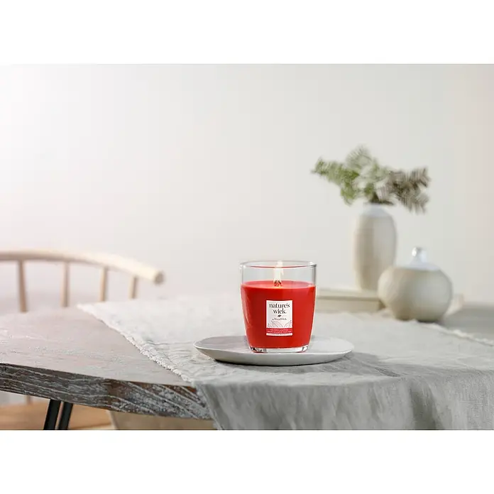 Woodwick Nature's Wick Duftkerze - Im Glas, Red Berry & Nutmeg, Anzahl Dochte: 1 Stk. - Ein rotes Nature's Wick Duftkerzenglas steht auf einem Tisch. Die Kerze ist entzündet und verbreitet einen angenehmen Duft.