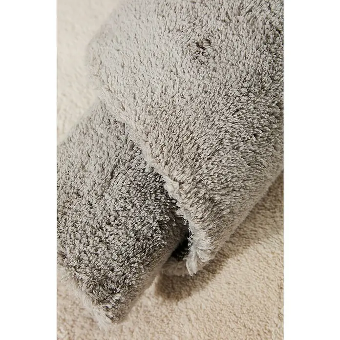 Alfombra de pelo corto Toscana - Plateado, 170 x 120 cm, 100% Poliéster - Primer plano de una alfombra de baño gris suave y enrollada que destaca su textura afelpada y su paleta de colores neutros.