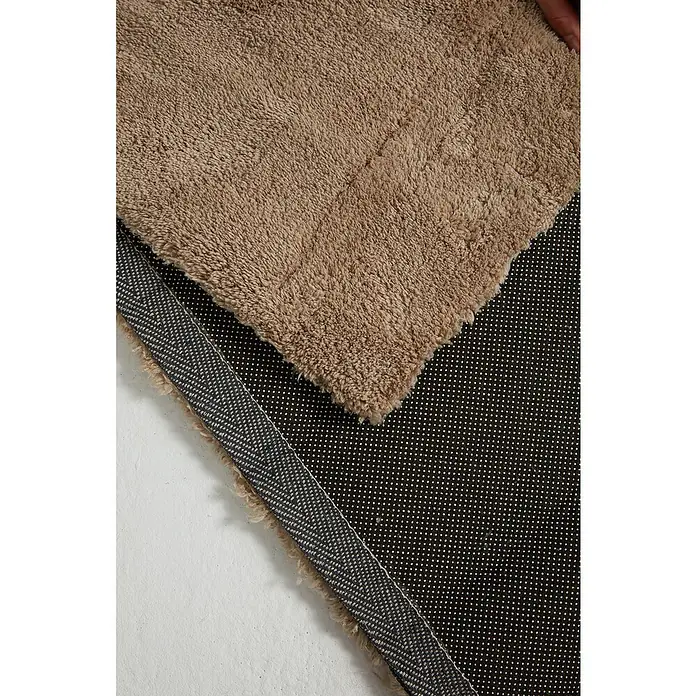 Alfombra de pelo corto Toscana - Beige, 300 x 200 cm, 100% Poliéster - Primer plano de una alfombra de baño beige con reverso antideslizante. La alfombra es suave y lujosa.