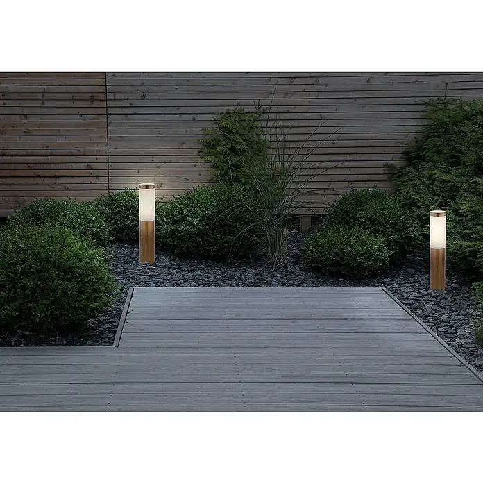 Globo Boston Sobremuro exterior - 60 W, Color del marco: Marrón, Sin bombillas - Luces de jardín de madera iluminan un camino pavimentado, rodeado de exuberante vegetación, creando un ambiente exterior cálido y acogedor.