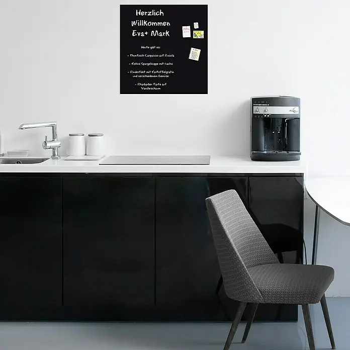 Magnetische Tafelfolie - Schwarz, 50 x 50 cm, Inkl. 3 Magnete und 3 Stück Kreide - Ein schwarzes Memoboard mit der Aufschrift "Herzlich Willkommen Eva+ Mark" hängt in einer modernen Küche mit minimalistischem Design.
