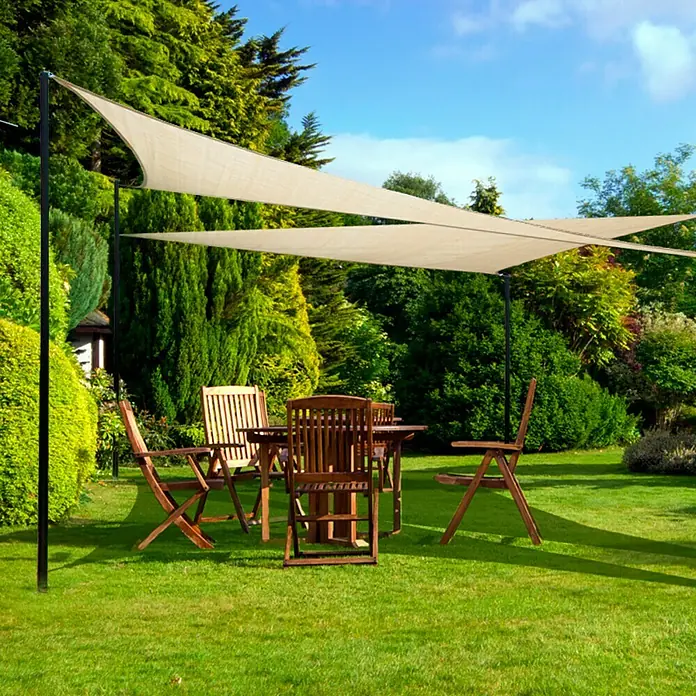 Sunfun SonnensegelSand, Dreieckig, L x B: 400 x 400 cm - Eine Gartenszene mit einem beigen Sonnensegel, das über einem Holztisch und Stühlen auf einem grünen Rasen gespannt ist, umgeben von üppigem Grün.