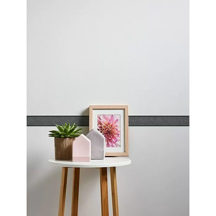A.S. Création Only Borders 11 Tapetenborte Streifen - Kunststoff, Schwarz/Grau - Weißer runder Beistelltisch mit hellen Holzbeinen, auf dem eine Sukkulente, ein gerahmtes Bild und zwei Hausfiguren stehen.