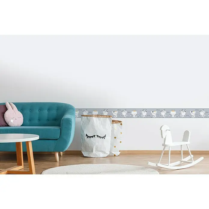A.S. Création Lovely Kids Tapetenborte - Kunststoff, Kätzchen Grau - Ein Kinderzimmer mit einer grauen Bordüre mit Katzenmotiven, einem blauen Sofa und einem weißen Schaukelpferd für eine spielerische Atmosphäre.