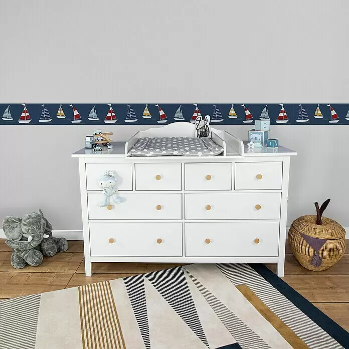 A.S. Création Lovely Kids Tapetenborte - Kunststoff, Segelschiffe - Weißer Wickelkommodenschrank aus Holz mit Holzknöpfen, grauer Wickelauflage und nautischer Dekoration im Kinderzimmer.