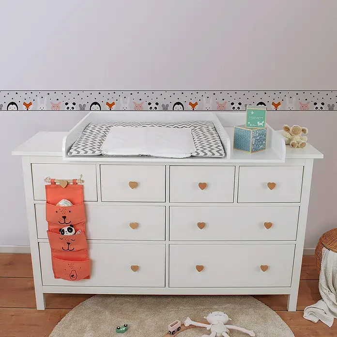 A.S. Création Lovely Kids Tapetenborte - Kunststoff, Tiere - Eine weiße Wickelkommode mit Herzgriffen und einem orangefarbenen Hängeorganizer, ideal für ein stilvolles und funktionales Kinderzimmer.