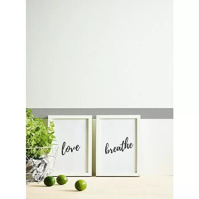 A.S. Création Only Borders 11 Tapetenborte Streifen - Kunststoff, Grau - Zwei weiße gerahmte Drucke mit "love" und "breathe" auf einer Holzfläche, flankiert von Pflanze und Limetten.
