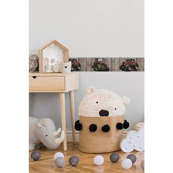 A.S. Création Only Borders 11 Tapetenborte Traktor - Kunststoff, Rot/Braun - Ein Kinderzimmer mit einem Bärenkorb, einem Schreibtisch und einer Girlande mit Kugeln. Die Wand ist mit Traktoren dekoriert.