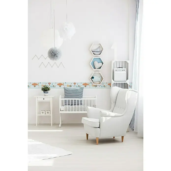 A.S. Création Lovely Kids Tapetenborte - Kunststoff, Luftparty - Ein helles Kinderzimmer mit einem weißen Sessel, einem Kinderbett und einer Bordüre mit Flugmotiven an der Wand.