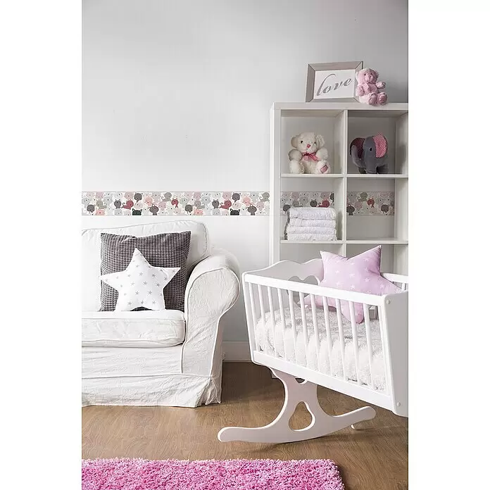 A.S. Création Lovely Kids Tapetenborte - Kunststoff, Kätzchen Rosa - Ein gemütliches Kinderzimmer mit weißem Sessel, Schaukelwiege, Regal mit Spielzeug und rosa Teppich auf Holzboden, verziert mit einer Katzentapetenborte.