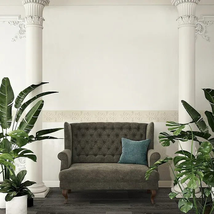A.S. Création Only Borders 11 Tapetenborte Edelstein - Edelstein Perlmutt, Selbstklebefolie - Eine elegante graue Couch mit Knopfheftung und einem blauen Kissen, umgeben von üppigen grünen Pflanzen und Säulen.