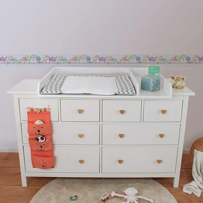 A.S. Création Lovely Kids Tapetenborte - Kunststoff, Vögel - Ein weißer Wickeltisch mit einem grauen Chevron-Muster und herzförmigen Knöpfen, darunter ein orangefarbener Organizer mit Bärenmotiven.