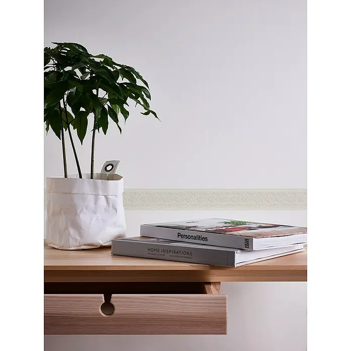 A.S. Création Only Borders 11 Tapetenborte OrnamentPerlmutt, 5 x 0,04 m, Selbstklebefolie - Zimmerpflanze in weißem Übertopf und zwei Büchern auf einem Holztisch mit Schublade für ein gemütliches Ambiente.