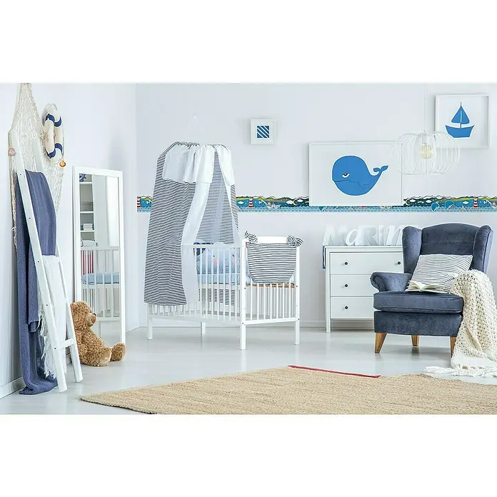 A.S. Création Lovely Kids Tapetenborte - Kunststoff, Wale mit Sternen - Ein maritimes Kinderzimmer mit einem weißen Kinderbett, einem blauen Sessel und nautischen Dekorationen, die eine ruhige und verspielte Atmosphäre schaffen.