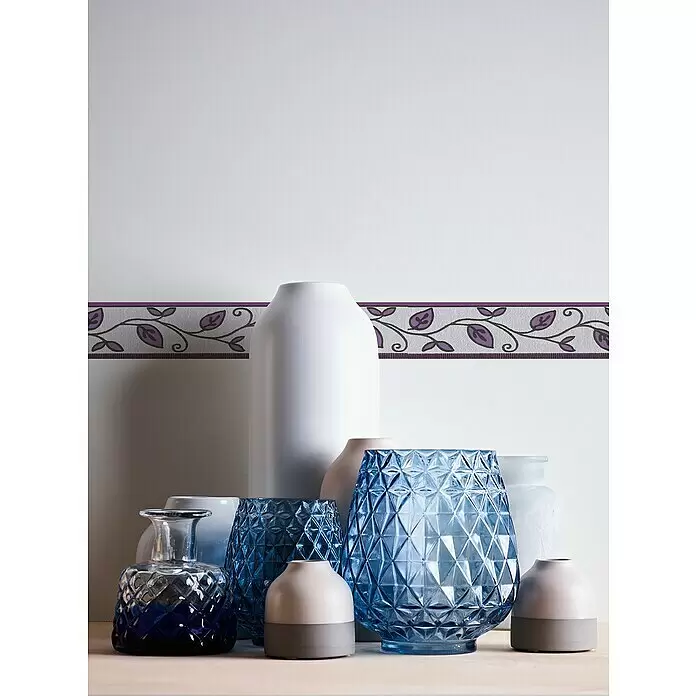 A.S. Création Only Borders 11 Tapetenborte Ranke - Kunststoff, Lila - Dekorative Vasen und Teelichthalter in Blau, Weiß, Dunkelblau und Pink, teils strukturiert, auf Holz unter einer gemusterten Wandborte.
