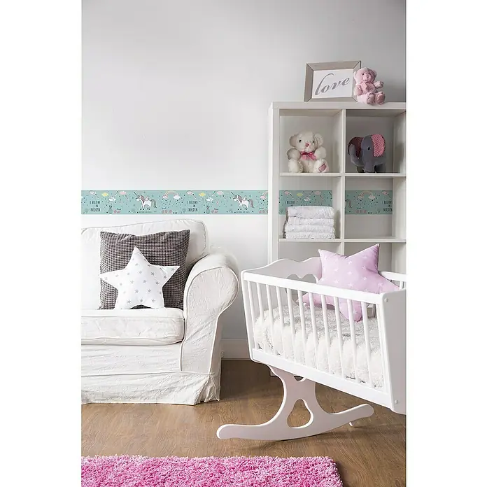 A.S. Création Lovely Kids Tapetenborte - Kunststoff, Einhorn - Blick in ein Kinderzimmer mit weißem Schaukelbett, Sofa und Regal, dekoriert mit Einhorn-Bordüre und Kuscheltieren für eine märchenhafte Atmosphäre.