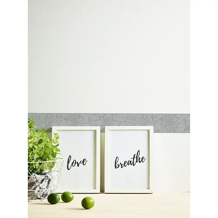 A.S. Création Only Borders 11 Tapetenborte Blume - Grau/Silber, 5 x 0,13 m, Selbstklebefolie - Eine Nahaufnahme von zwei gerahmten Kunstdrucken mit den Worten "Liebe" und "Atmen" vor einer grauen Bordüre.