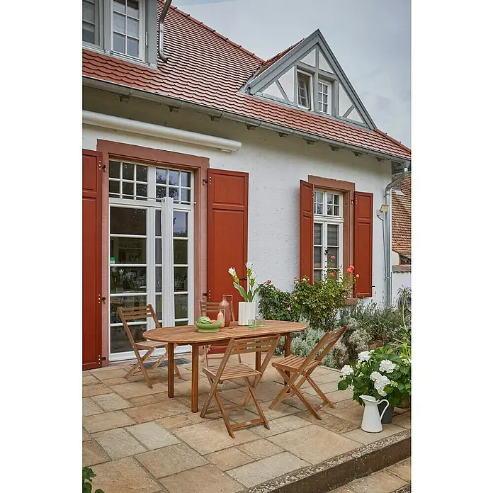 Sunfun Gartenmöbel-Set Diana - 5 -tlg., Akazienholz, Niederlehner ohne Armlehne, Tischplatte ausziehbar - Ein Gartentisch-Set aus Holz steht auf einer Steinterrasse vor einem charmanten Haus, ideal für Mahlzeiten im Freien und gesellige Stunden.