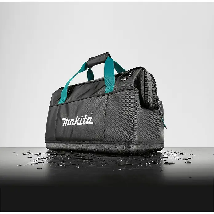 Makita Werkzeugtasche E-15425 - L x B x H: 510 x 295 x 280 mm, 34 l, Ohne Werkzeug - Nahaufnahme einer Makita Werkzeugtasche mit grünen Griffen auf einer nassen, glänzenden Oberfläche vor einem hellen Hintergrund.