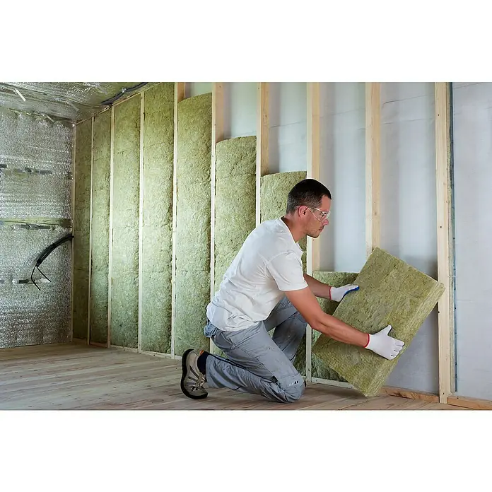 Rockwool Steinwolle Sonorock Akustik Trennwandplatte - Stärke: 45 mm, Wärmeleitfähigkeit: 0,04 W/(mK) - Ein Handwerker kniet und bringt ein rechteckiges Dämmstoffstück zwischen Holzrahmen an, um die Wand zu isolieren.