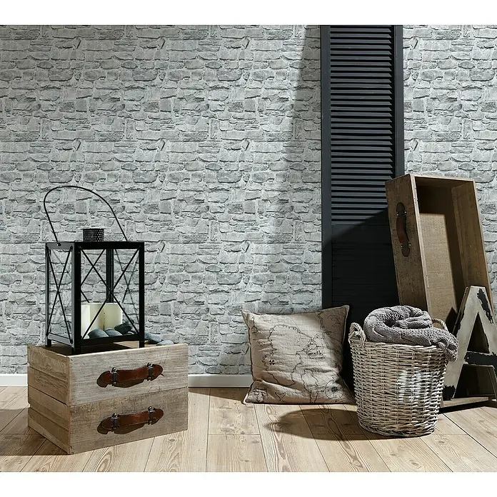 A.S. Création Il Decoro Vliestapete Bruchsteinmauer - Grau, Steinoptik, 10,05 x 0,53 m - Nahaufnahme eines Raumes mit rustikalen Dekorationsgegenständen, darunter eine Laterne, Kissen und Körbe auf einem Holzboden.