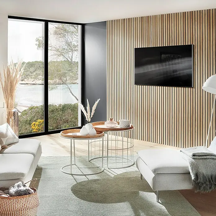 Panel de pared Linari - 120 x 50 cm, 2 ud. - Salón con sofá luminoso, mesas de centro y TV montada en una pared de paneles de madera. La habitación ofrece una vista de una costa escénica.