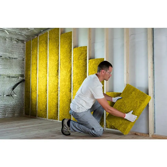 Probau Glaswolle Trennwandplatte TWP1 - Stärke: 100 mm, Wärmeleitfähigkeit: 0,039 W/(mK) - Ein Handwerker montiert gelbe Isolierwolle an einer Wand, um die Wärmeisolierung des Hauses zu verbessern. Schutzkleidung inklusive.