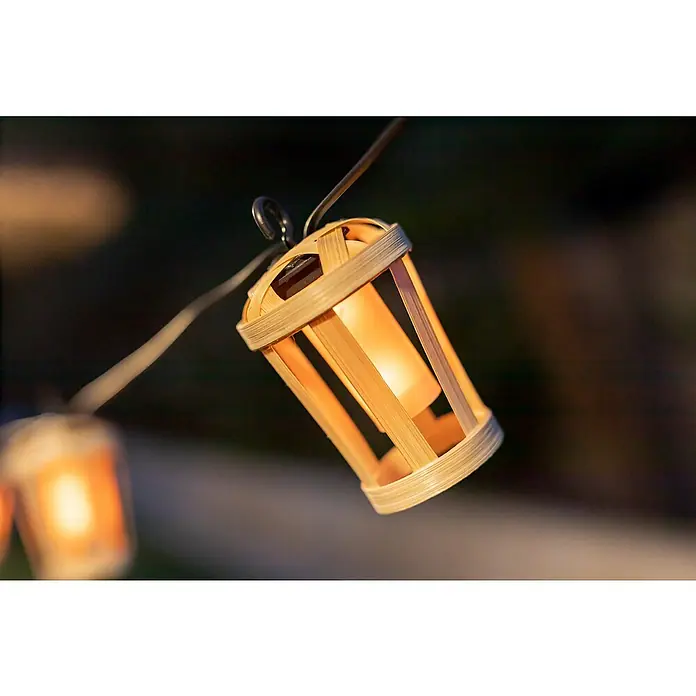 New Garden Guirnalda luminosa LED Hiama - 3 W, 50 lm, Bambú, 5 m, IP44 - Primer plano de una linterna decorativa de bambú, suspendida de una cadena de luces, que emite un brillo cálido y acogedor.