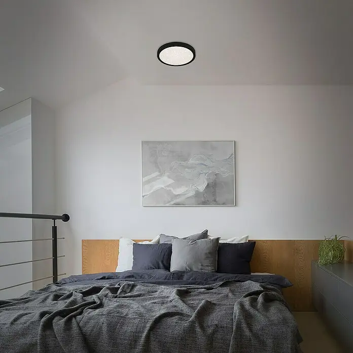 Briloner LED-Deckenleuchte rund RUNA - 18,5 W, Ø x H: 28 x 4 cm, Schwarz, Neutralweiß - Nahaufnahme einer modernen runden Deckenleuchte mit schwarzem Rand, die ein helles, gleichmäßiges Licht in einem Schlafzimmer ausstrahlt.