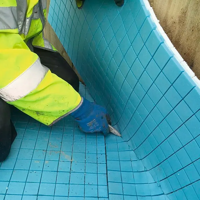 Lámina de drenaje Espuma - 1,5 x 1,5 m, Azul - Artesano cortando paneles de aislamiento azules a medida para un proyecto de construcción. Los paneles son cuadrados y cuadriculados.