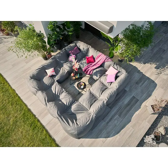 Loungesofa Modul - 107 x 107 x 72 cm, Polyesterfaser, Grau, Eckelement - Luftaufnahme eines grauen modularen Sofas mit Kissen und Decke im Freien, umgeben von Pflanzen und Fliesenboden.