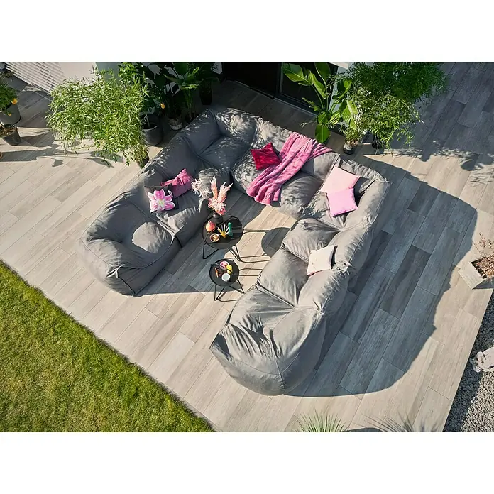 Loungesofa Modul - 107 x 107 x 72 cm, Polyesterfaser, Grau, Eckelement - Luftaufnahme eines modularen grauen Sofas mit Kissen und Decke auf einer Terrasse, umgeben von Pflanzen.