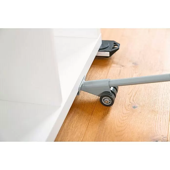 Wagner System Transportroller - Traglast: 150 kg, Stahl - Grauer Möbelheber hebt weißes Möbelstück auf Holzfußboden, mit einem schwarzen Möbelroller darunter.