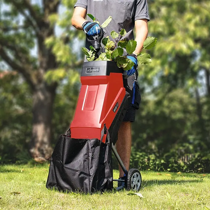 Scheppach Elektro-Häcksler GS55 - Max. Aststärke: 4,5 cm, 2.400 W - Ein Mann benutzt einen Scheppach Gartenhäcksler, um Äste zu zerkleinern. Der Häcksler steht auf einem Rasen und hat einen schwarzen Auffangsack.