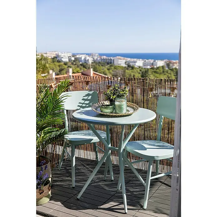 Silla de jardín Abigail - 47 x 52 x 83 cm, Verde claro, Aluminio, Apilable - Un conjunto de bistro verde menta con una mesa y sillas está en un balcón con vista al mar. Elementos decorativos como velas y plantas.