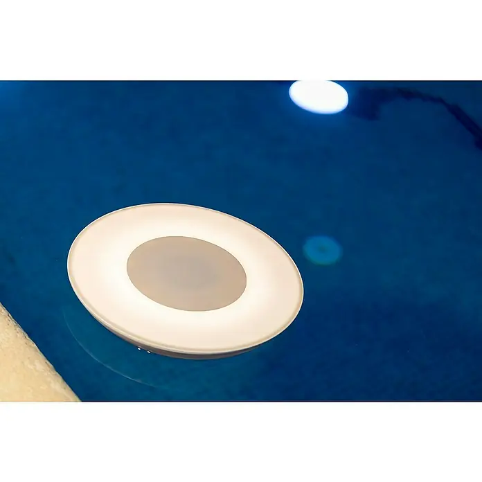 New Garden LED-Poolbeleuchtung mit Bluetooth Lautsprecher Wally Play - Durchmesser: 38 cm, Weiß, LED - Nahaufnahme einer runden, schwimmenden Poolleuchte mit weißem Rand und grauem Zentrum im blauen Wasser. Sie sorgt für stimmungsvolle Beleuchtung im Pool.