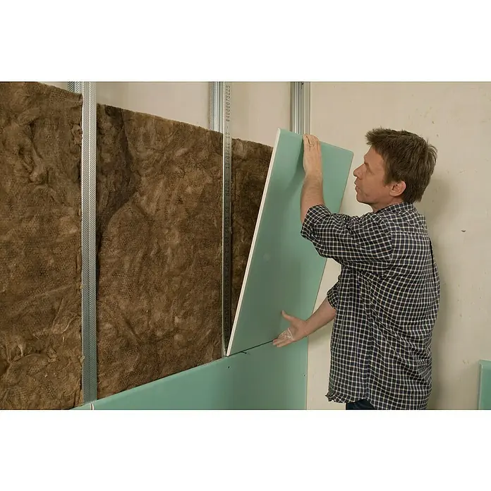 Knauf Gipskartonplatte Top 2000 GKFI - 1.250 x 900 x 12,5 mm, Imprägniert - Ein Mann montiert eine grüne Gipskartonplatte an einer Wand mit Isolierung und Metallrahmen. Die Platte wird passgenau angebracht.