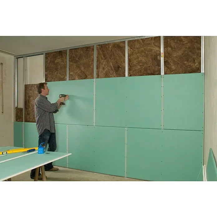 Knauf TOP 2000 Verbundplatte EPS - 1.250 x 900 x 33 mm - Ein Mann befestigt eine grüne Gipskartonplatte an einer Wand mit Isolierung und Metallrahmen mit einem Akkuschrauber.