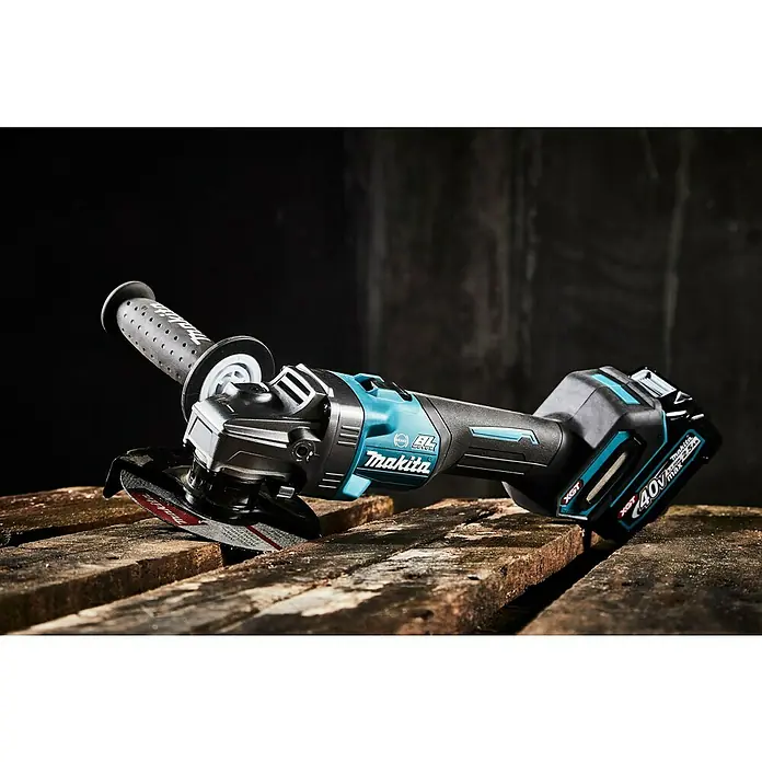 Makita XGT 40V max. Akku-Winkelschleifer GA005GM201 - 2 Akkus, 4 Ah, Leerlaufdrehzahl: 8.500 U/min - Nahaufnahme eines Makita Akku-Winkelschleifers mit Seitengriff und 40V Akku auf einer Holzoberfläche.