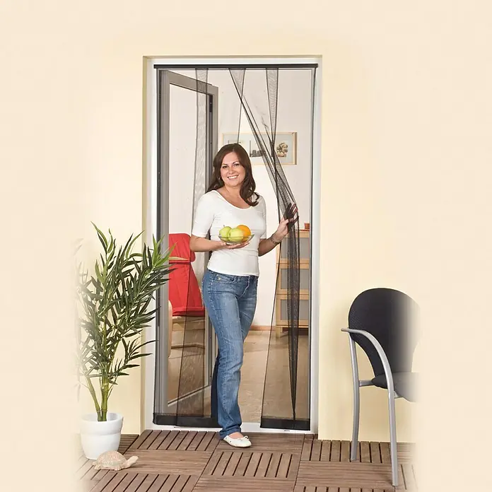 Easy Life Insektenschutzvorhang - B x H: 100 x 220 cm, Montage Insektengitter: Klemmen - Eine Frau geht durch eine magnetische Fliegengittertür, die Insekten fernhält und frische Luft hereinlässt.