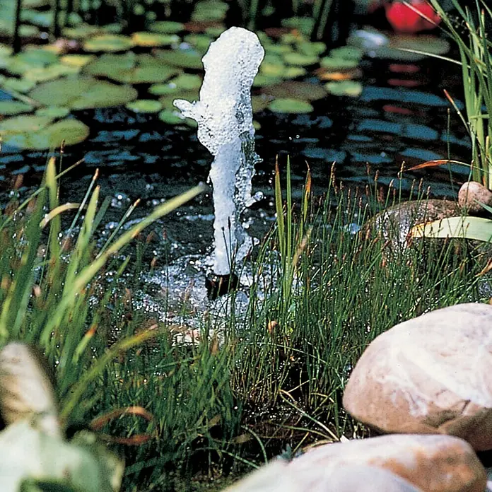 Ubbink Wasserspielpumpe Elimax 2000 - 35 W, Max. Förderhöhe: 220 cm - Nahaufnahme eines sprudelnden Springbrunnens in einem Teich, umgeben von Grün und Steinen, der Ruhe und natürliche Schönheit ausstrahlt.