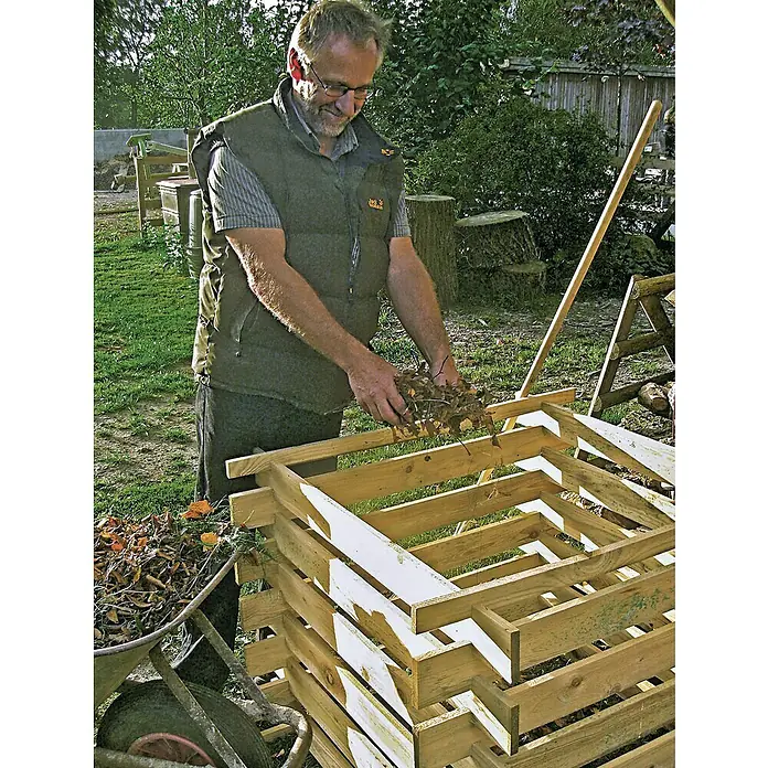T & J Komposter Bodo - 700 l, 100 x 100 x 70 cm - Ein Mann befüllt einen hölzernen Kompostbehälter mit Laub, um organischen Dünger für den Garten herzustellen.